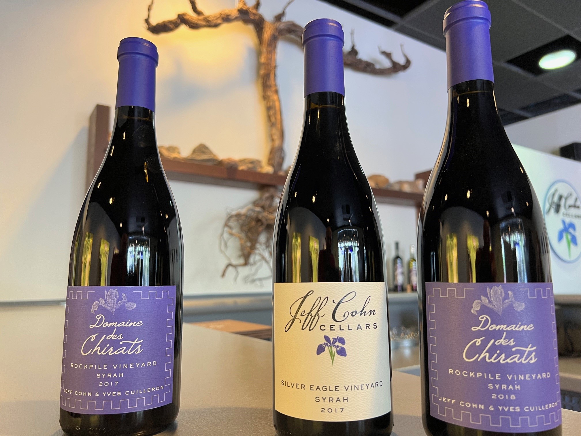 Bottles of Jeff Cohn Cellars Wines domaine des Chirats Syrah in the Tasting Room with vine in the background