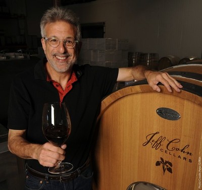 Jeff cohn smiling holding a glass of wine with his arm resting on a wooden barrel