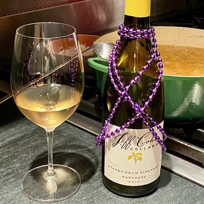Stagecoach Marsanne in a glass next to a bottle draped in purple Mardi Gras beads on the counter next to a Dutch oven with Shrimp Gumbo on the stove